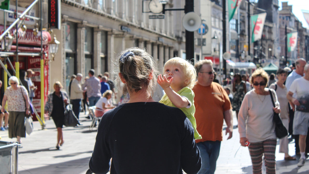 Young child in adults arms being carried looking up the sky in city