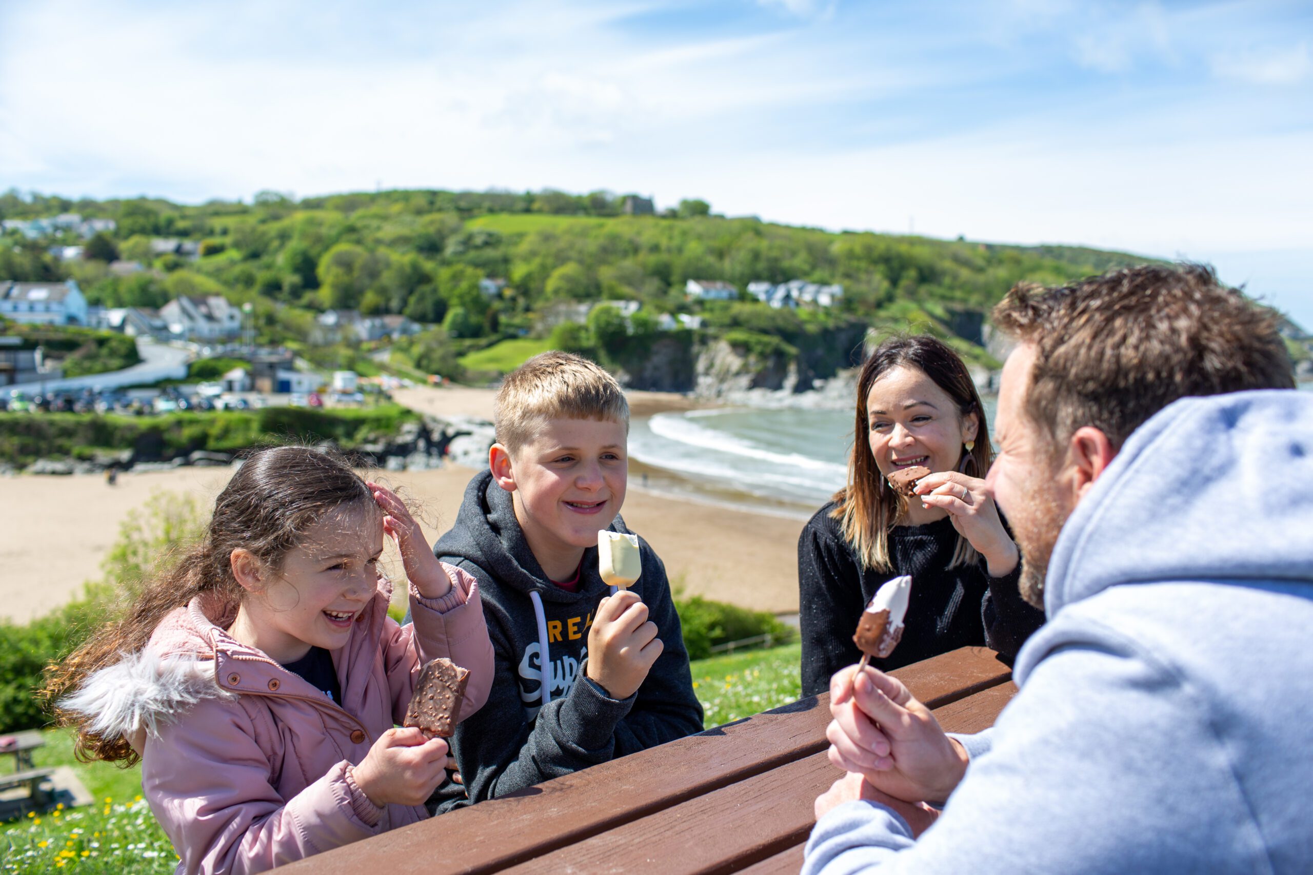 Two adults and two children eating ice-cream overlooking bay in Ceredigion
