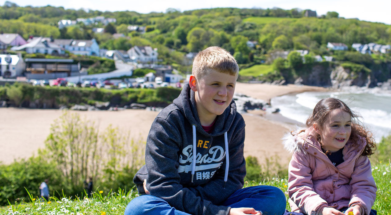 Two children sitting on cliffs with bay behind in sun