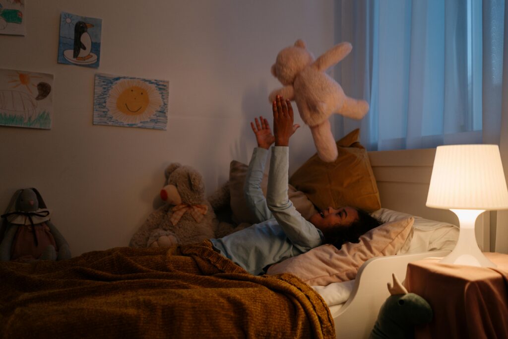 girl lying on bed throwing her teddy in the air