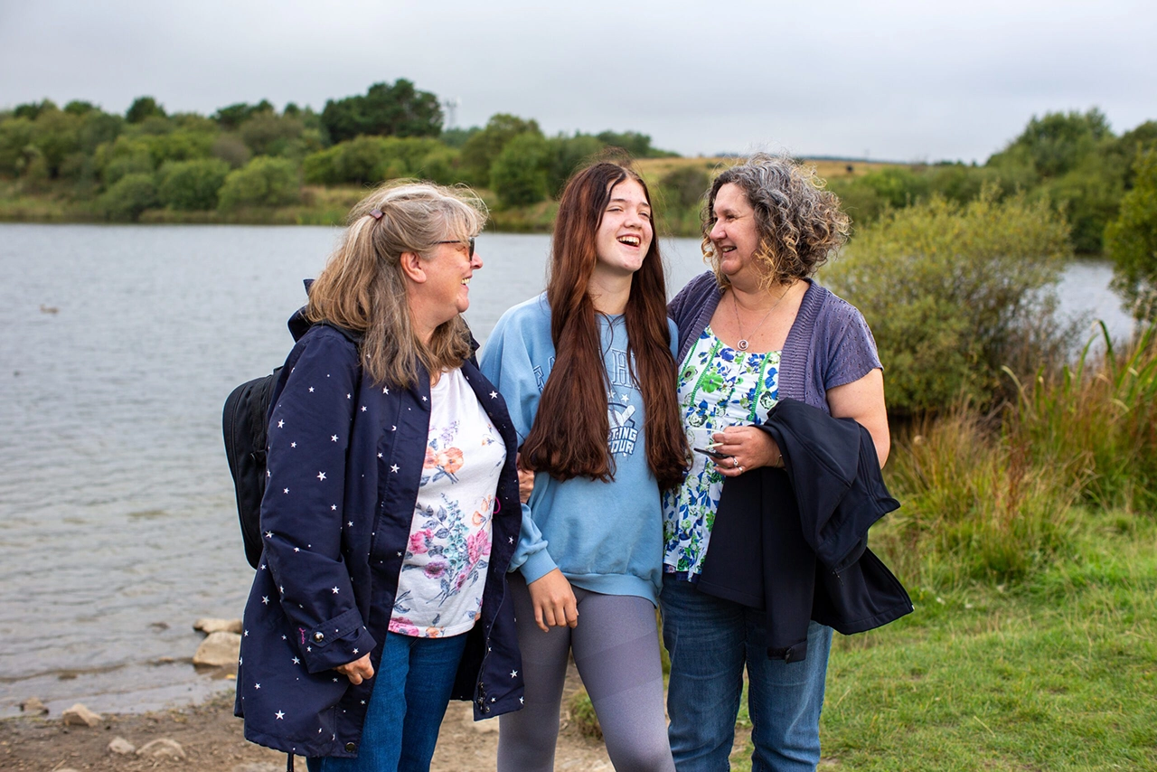 Two ladies and teenage girl laughing outdoors beside a lake