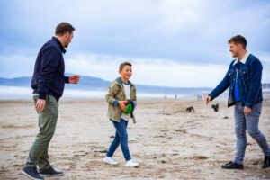 Boy and male couple on beach playing rugby